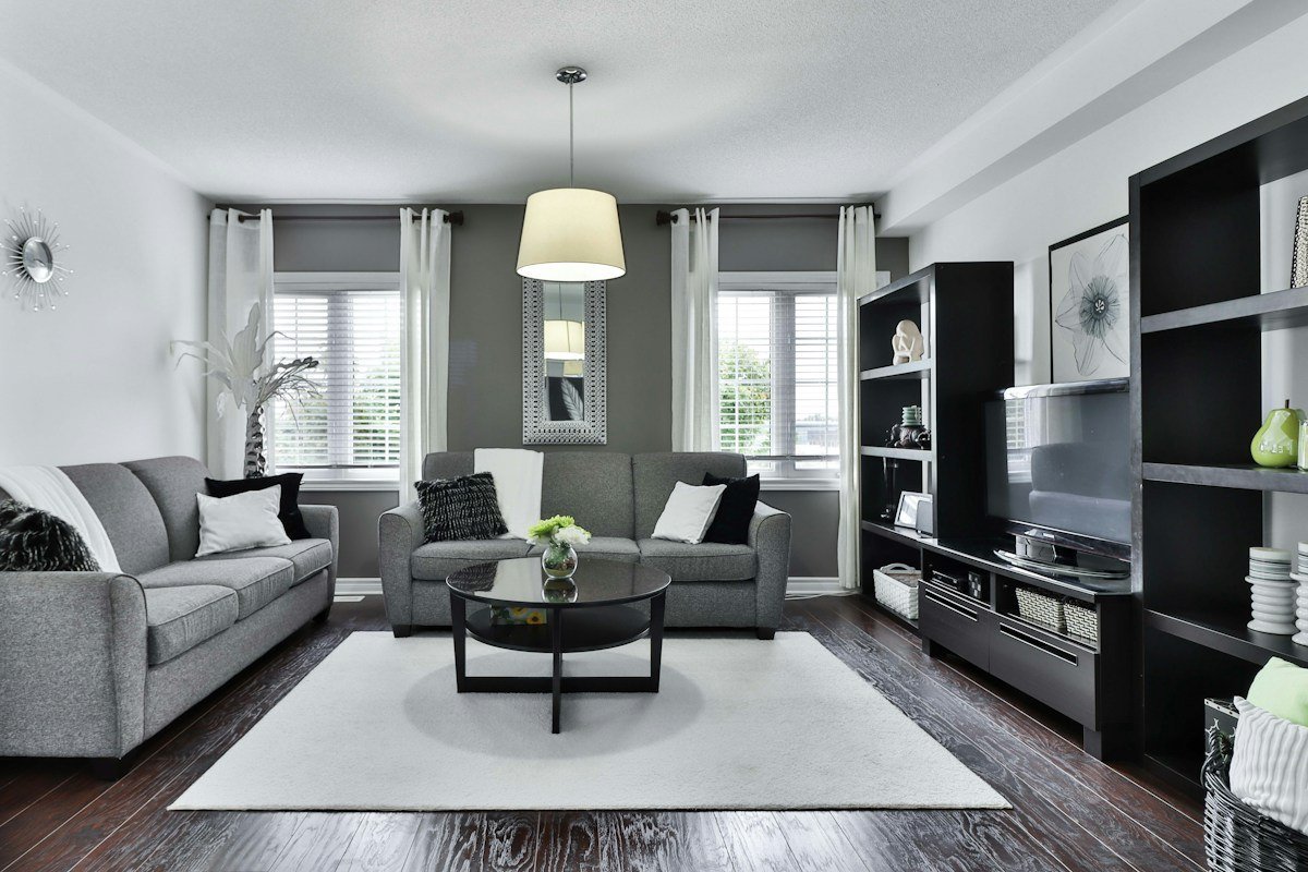 Real living room photograph with side walls, a back accent wall, grey sofas and windows